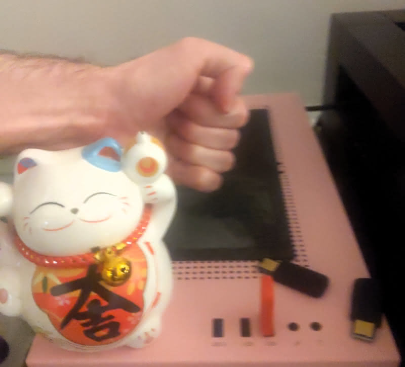 A fist overs over the top of a pink desktop computer behind a lucky cat.